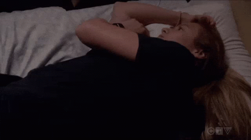 A Woman In A Black Shirt Is Laying On A Bed With Her Arms Crossed . GIF