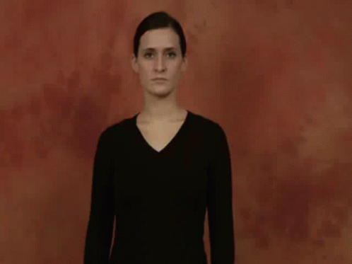 A Woman In A Black Shirt Is Making A Hand Gesture With Her Hands . GIF