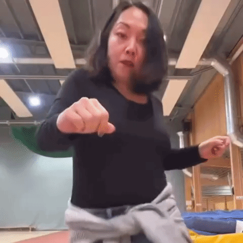 A Woman In A Black Shirt Is Pointing Her Finger At The Camera . GIF