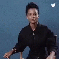 A Woman In A Black Shirt Is Sitting In A Chair With A Twitter Bird Flying In The Background . GIF