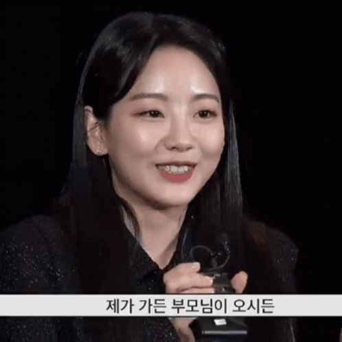 A Woman In A Black Shirt Is Smiling And Holding A Microphone With Korean Writing On The Bottom GIF