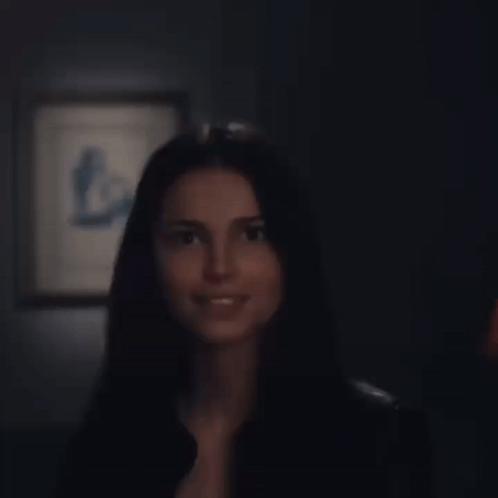 A Woman In A Black Shirt Is Smiling In Front Of A Framed Picture GIF