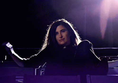 A Woman In A Black Shirt Is Standing In A Dark Room GIF