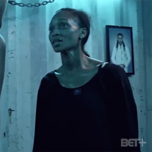 A Woman In A Black Shirt Is Standing In A Room With A Picture Of A Woman On The Wall . GIF
