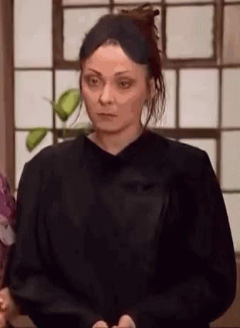 A Woman In A Black Shirt Is Standing In Front Of A Window And Looking At The Camera . GIF
