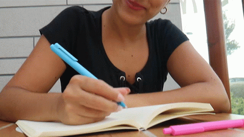 A Woman In A Black Shirt Is Writing In A Notebook GIF