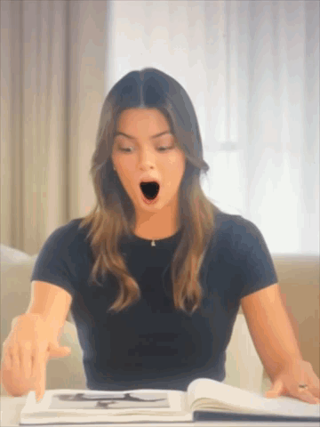 A Woman In A Black Shirt Is Yawning While Reading A Book GIF