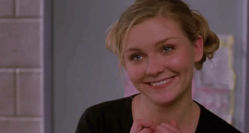 A Woman In A Black Shirt Looks At The Camera And Smiles GIF