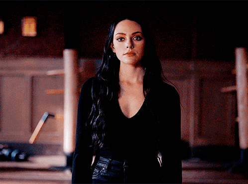 A Woman In A Black Shirt Stands In A Dark Room GIF