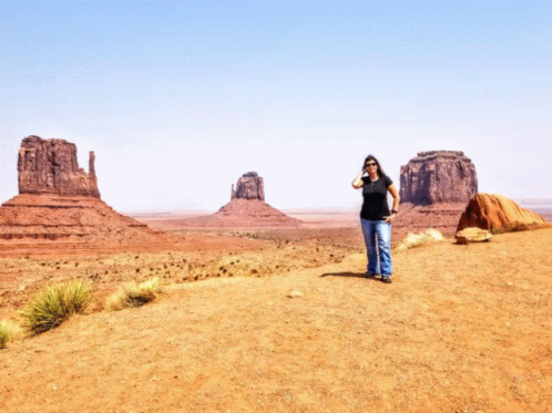 A Woman In A Black Shirt Stands On A Dirt Road In The Desert GIF