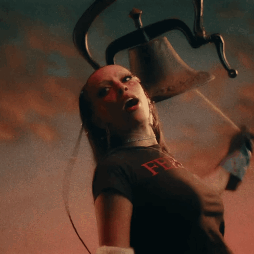 A Woman In A Black Shirt With The Letter F On It Holds A Bell GIF