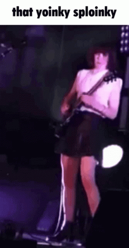 A Woman In A Black Skirt Is Playing A Guitar On Stage . GIF