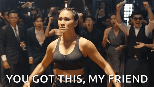 a woman in a black sports bra stands in front of a crowd and says you got this my friend