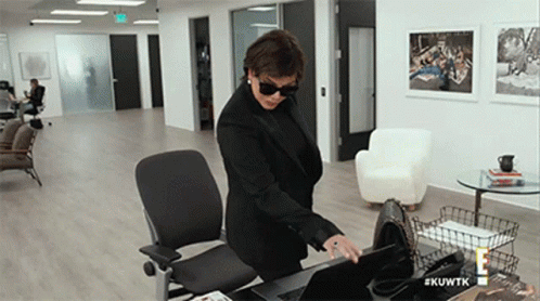 A Woman In A Black Suit And Sunglasses Is Standing At A Desk With A Laptop .. GIF
