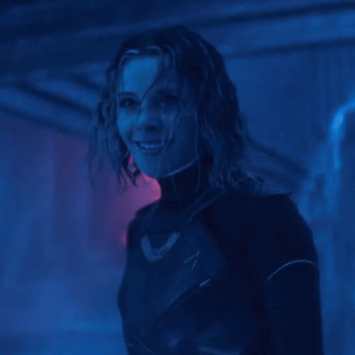 A Woman In A Black Suit Is Smiling In A Dark Room GIF