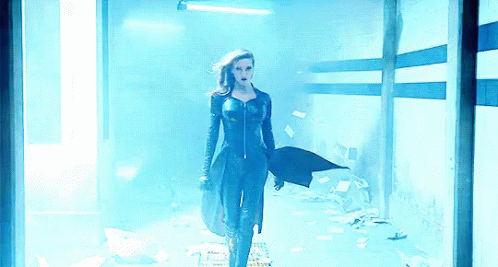 A Woman In A Black Suit Is Standing In A Dark Room GIF