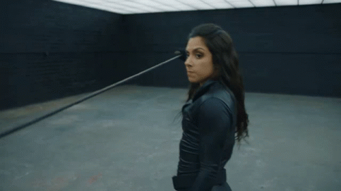 A Woman In A Black Suit Is Standing In A Dark Room With Her Arms Outstretched GIF