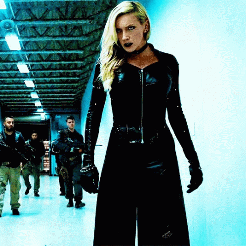 A Woman In A Black Suit Is Standing In A Hallway With A Group Of Men GIF
