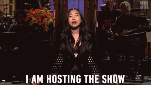 A Woman In A Black Suit Is Standing On A Stage And Says I Am Hosting The Show . GIF