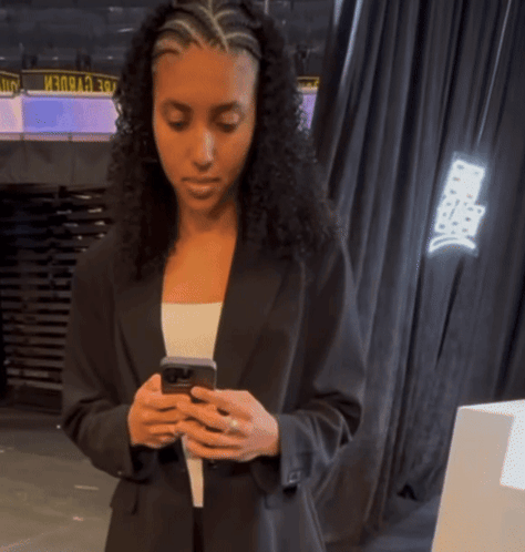 A Woman In A Black Suit Looks At Her Phone GIF