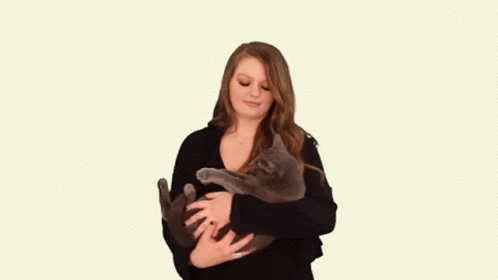 A Woman In A Black Sweater Is Holding A Gray Cat In Her Arms . GIF