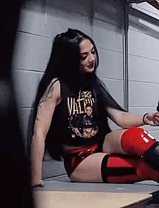 A Woman In A Black Tank Top And Red Shorts Is Sitting On A Bench . GIF