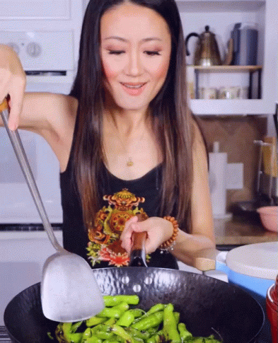 A Woman In A Black Tank Top Is Cooking Green Beans In A Wok GIF