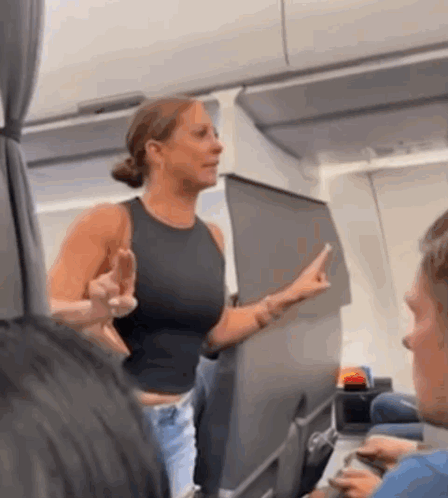 A Woman In A Black Tank Top Is Giving The Middle Finger On An Airplane GIF