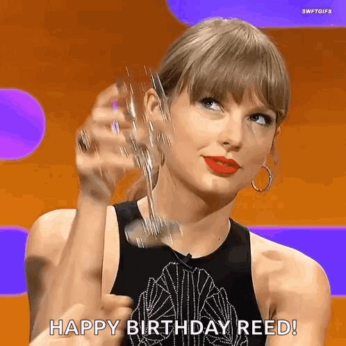 A Woman In A Black Tank Top Is Holding A Glass Of Champagne And Saying `` Happy Birthday Reed '' . GIF