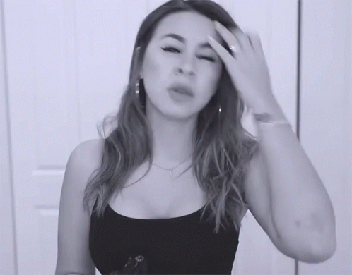 A Woman In A Black Tank Top Is Holding Her Head GIF
