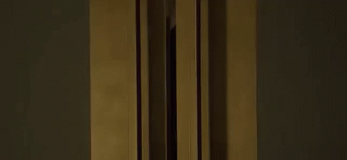 A Woman In A Black Tank Top Is Standing In Front Of A Window . GIF