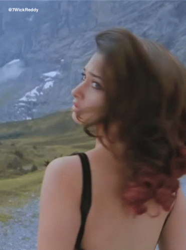 A Woman In A Black Tank Top Is Standing In Front Of Mountains GIF