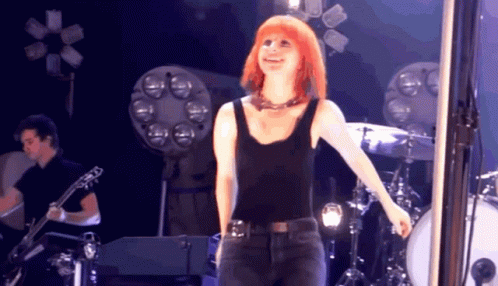 A Woman In A Black Tank Top Is Standing On Stage GIF