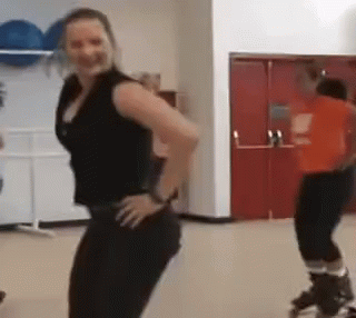 A Woman In A Black Tank Top Is Standing With Her Hands On Her Hips In A Gym GIF