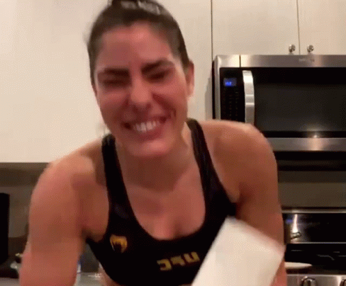 A Woman In A Black Tank Top With The Word Ufc On It Is Smiling In Front Of A Microwave . GIF