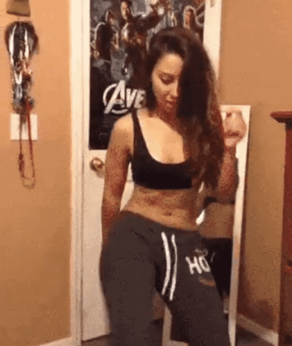 A Woman In A Black Top And Grey Sweatpants Is Dancing In Front Of A Mirror In A Room . GIF
