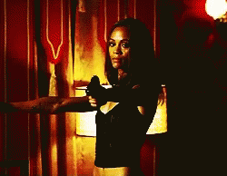 A Woman In A Black Top Is Holding A Gun GIF