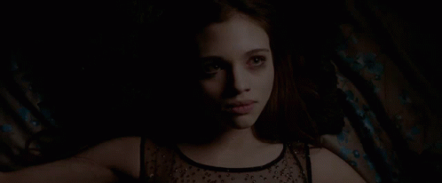 A Woman In A Black Top Is Laying Down In The Dark GIF
