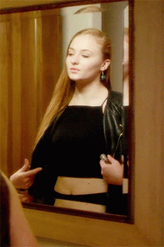 A Woman In A Black Top Is Looking At Herself In The Mirror GIF