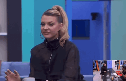 A Woman In A Black Top Is Sitting At A Table With A Cup Of Coffee GIF