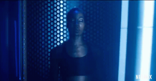 A Woman In A Black Top Is Standing In A Dark Room With A Blue Light Shining On Her Face . GIF