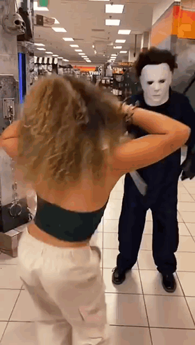 a woman in a black top is standing next to a man in a mask in a store .