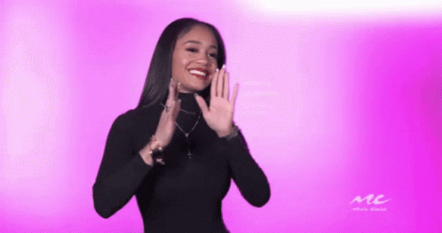 A Woman In A Black Turtleneck Is Clapping Her Hands In Front Of A Pink Background GIF