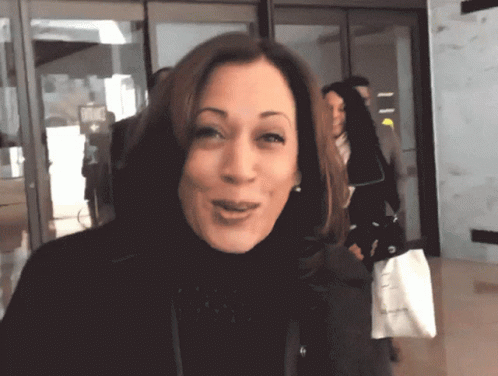 A Woman In A Black Turtleneck Is Smiling And Holding A White Bag That Says ' Calvin Klein ' On It GIF