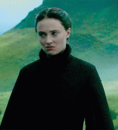 A Woman In A Black Turtleneck Is Standing In A Field GIF