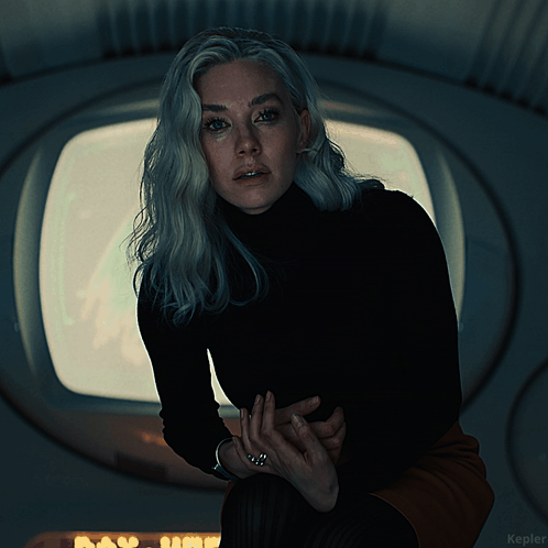 A Woman In A Black Turtleneck Stands In Front Of A Window With The Word Kepler On The Bottom Right GIF