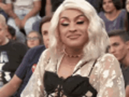 A Woman In A Blonde Wig Is Sitting In A Crowd Of People . GIF