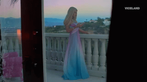 A Woman In A Blue And Pink Dress Is Standing On A Balcony With The Word Viceland On The Bottom Right GIF