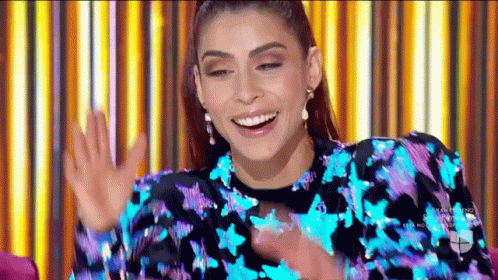 A Woman In A Blue And Purple Sequined Dress Is Smiling And Waving Her Hands . GIF