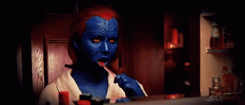 A Woman In A Blue And Red Costume Is Brushing Her Teeth In Front Of A Mirror . GIF